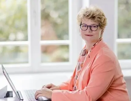 Bild der Inhaberin vor einem Laptop. Im Hintegrund ein Fenster mit Blick in einen Garten im Sommer.